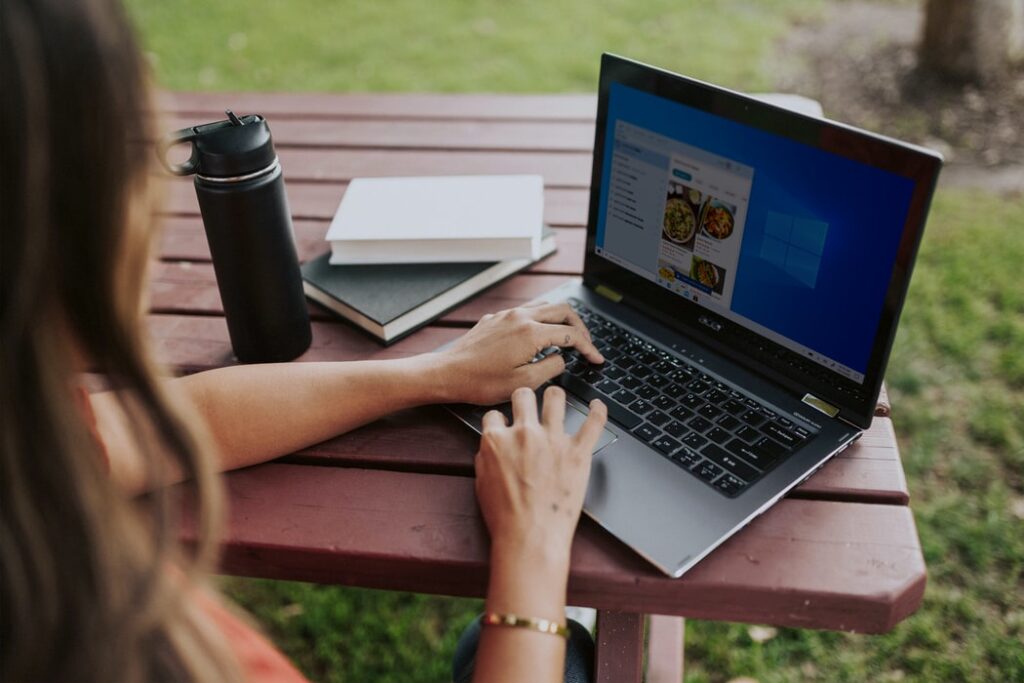 Image of laptop on picnic table with woman, water bottle and books